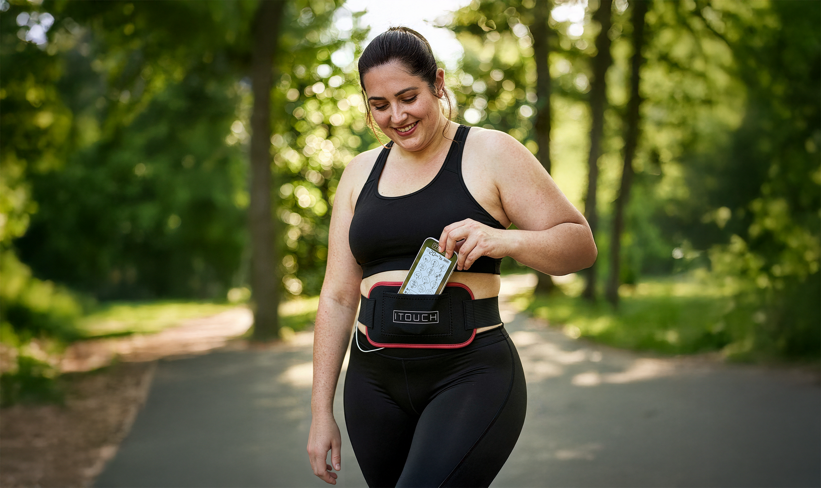Woman wearing the ITOUCH belt outdoors, placing the Touch X device into the built in pouch for hands free use.
